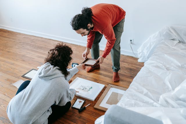 A couple arranging artwork on the floor of their new home.