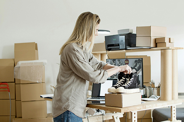 Woman holding black shoes on top of the cardboard box.