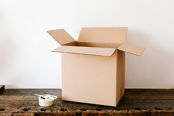 Cardboard box on a wooden surface right next to scissors and a duck tape